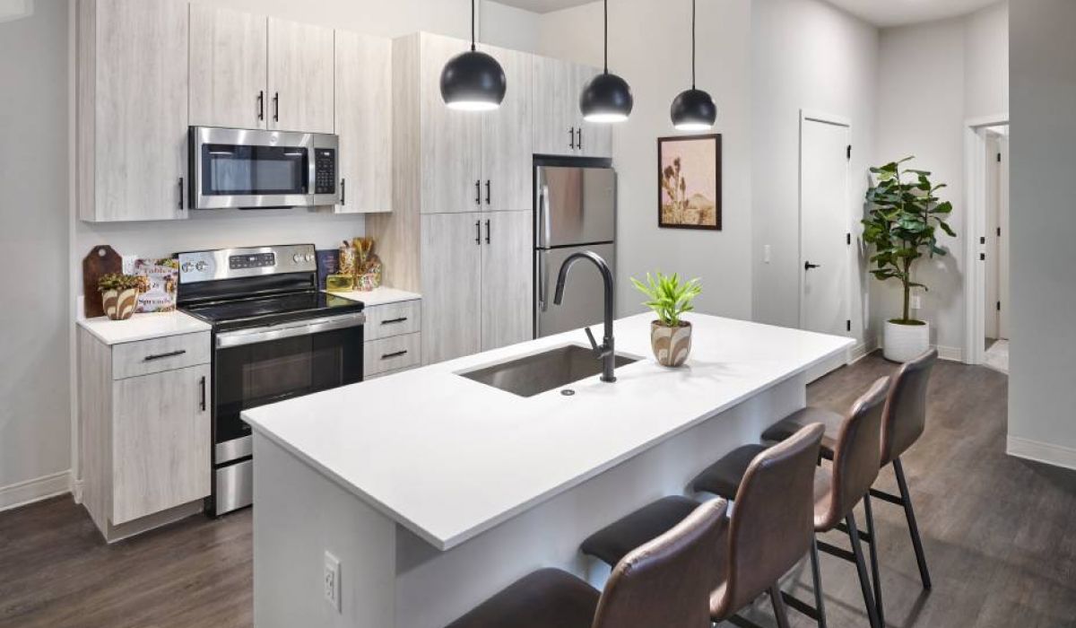 A modern kitchen in VERVE Boise with light wood cabinetry, stainless steel appliances, an island with bar seating, and pendant lighting.